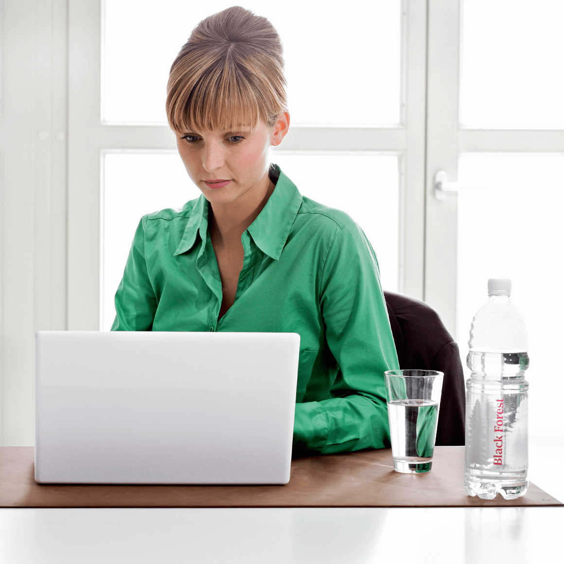 Junge Frau am Laptop trinkt Black Forest still